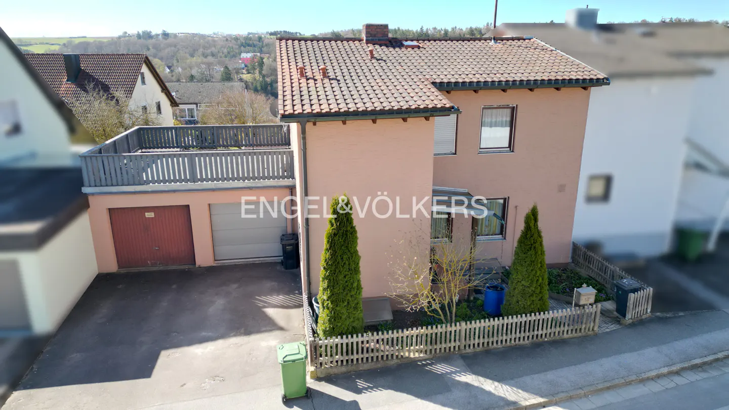 Two-story peach house with a brown tiled roof, two-car garage, and a wooden fence. Engel & Völkers logo is visible.