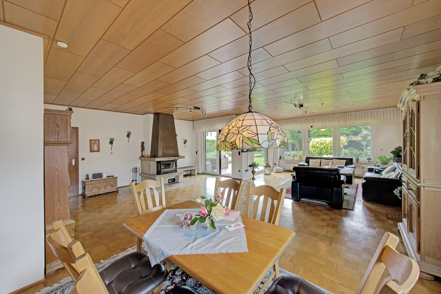 Spacious living and dining room with wood-paneled ceiling, fireplace, stained-glass pendant light, and parquet flooring.