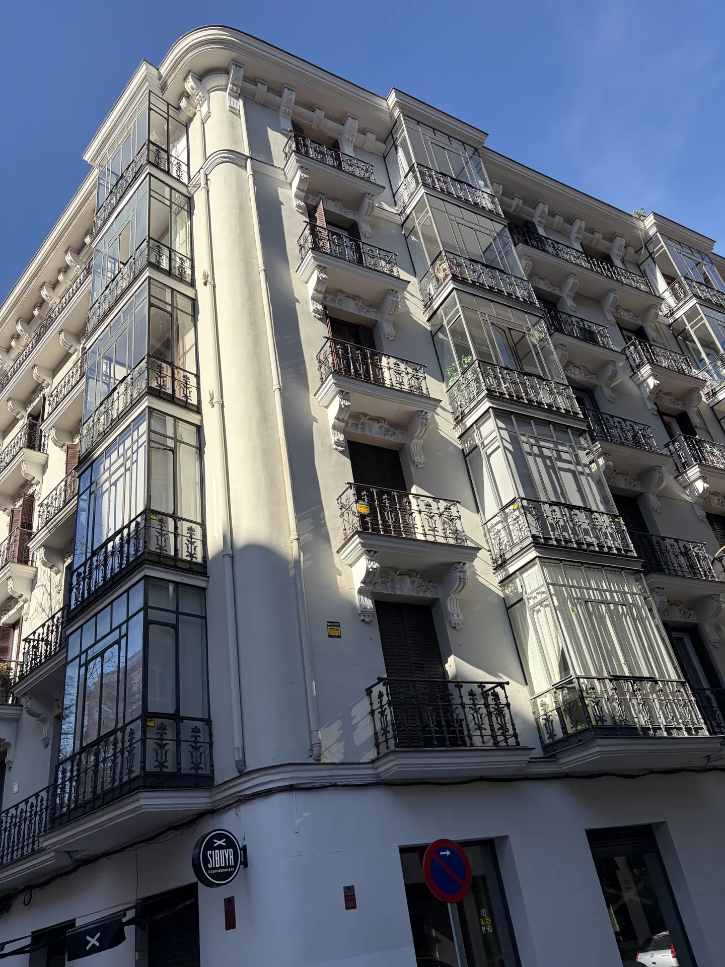 Exterior view of a multi-story white building with glass enclosed balconies and wrought iron railings under a blue sky.