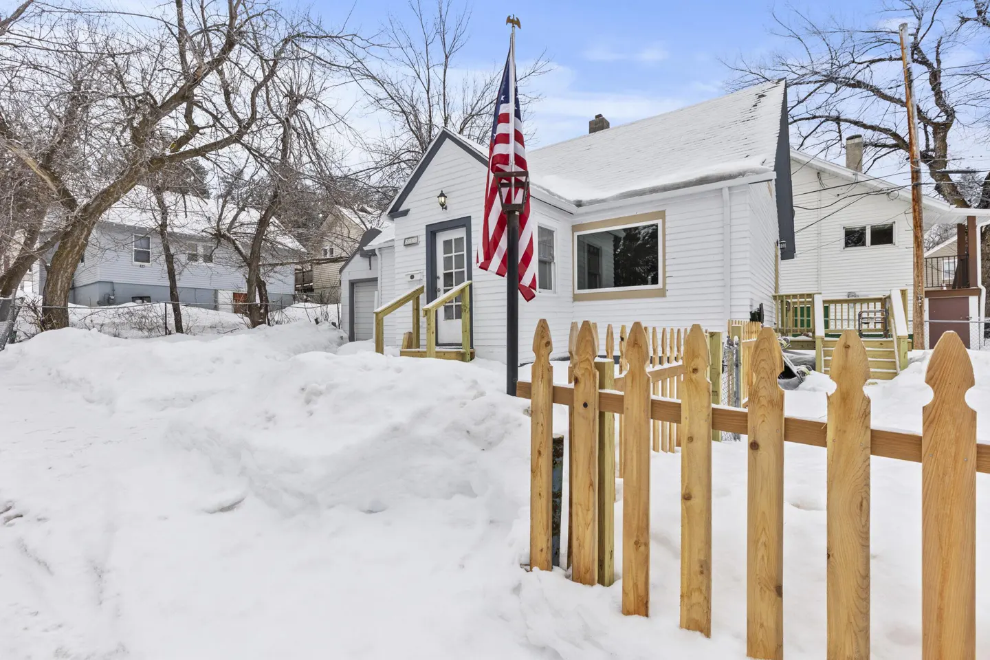Exterior view of a white house with a picket fence and an American flag in a snowy yard.