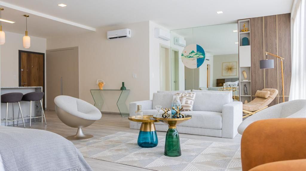 Bright, modern living room with white sofa, round chairs, and colorful glass tables on a geometric rug. A large mirror reflects the space.