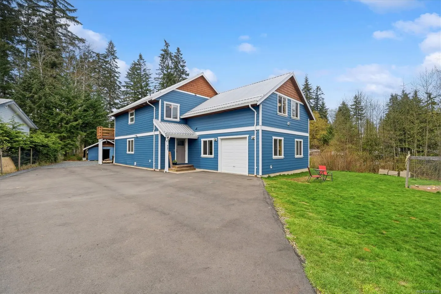 Two-story blue house with white trim, a gray roof, and a white garage door. A green lawn and trees surround the house.