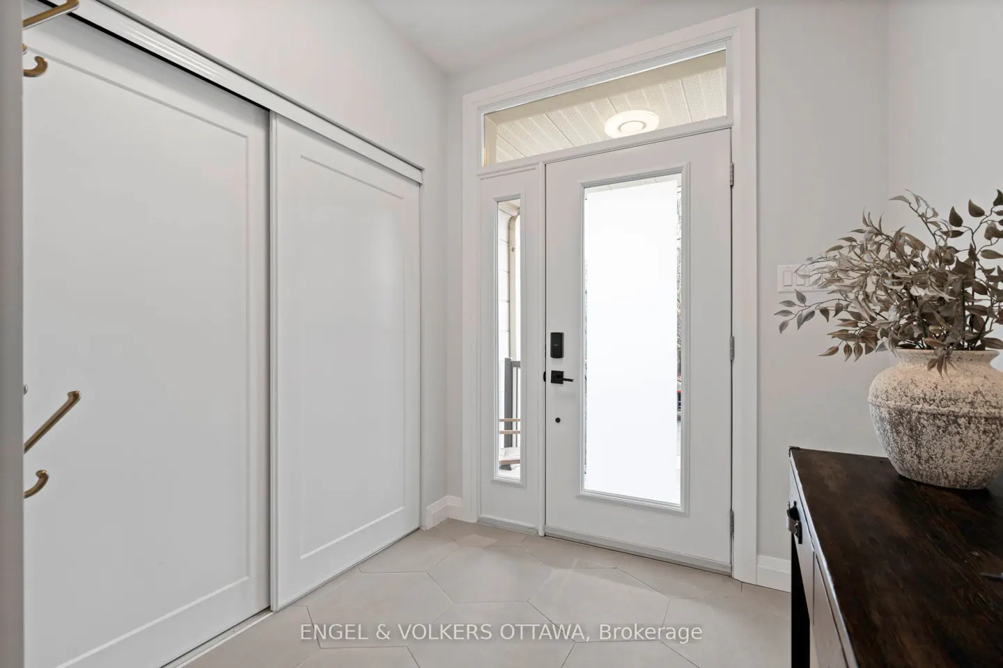 Bright entryway with white sliding closet doors, a white front door with frosted glass, and a dark wood console table with a decorative vase.