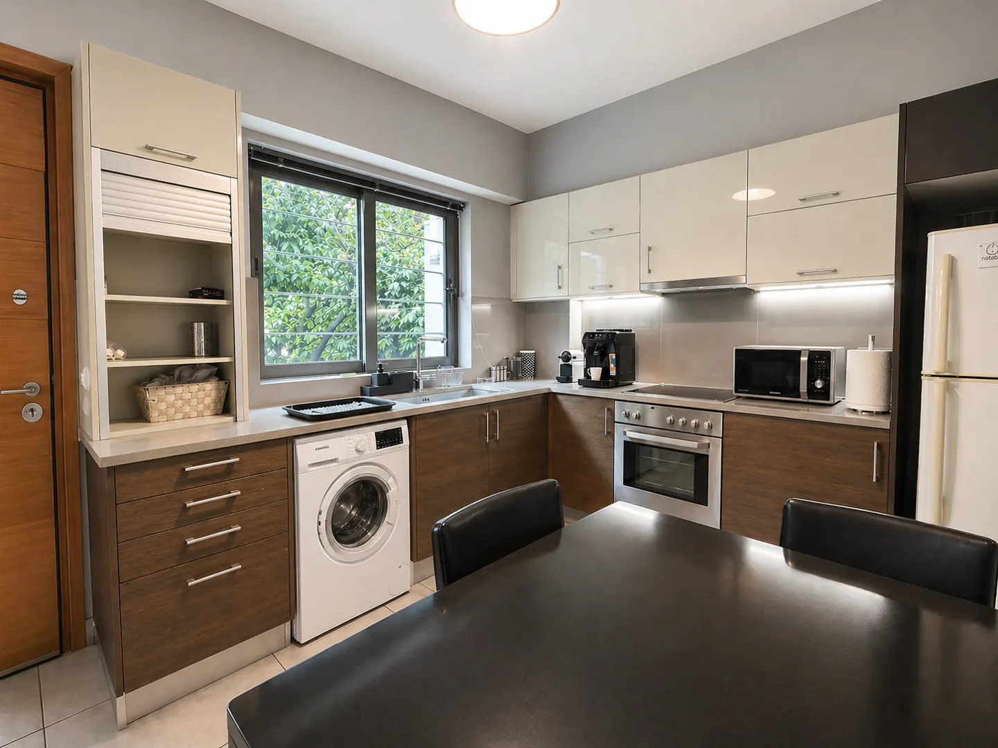 Modern kitchen with white cabinets, stainless steel appliances, and a washing machine. A black dining table is in the foreground.