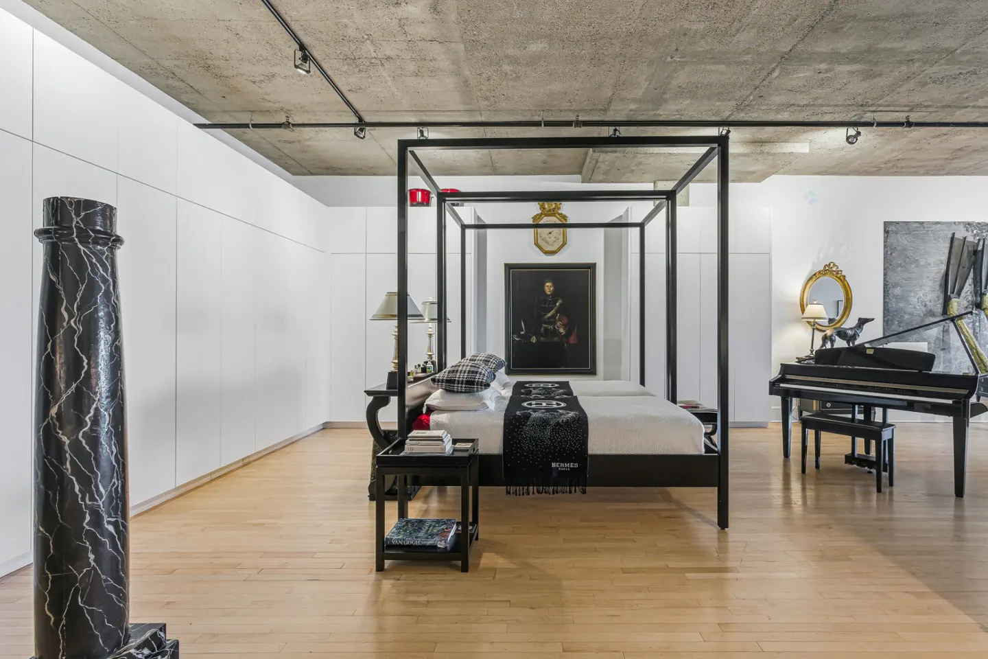 A modern bedroom with a black four-poster bed, piano, and marble column.