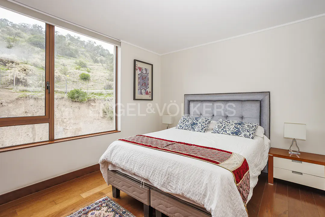 Bedroom with a large window showing a hillside, a bed with a gray headboard, and a wooden floor.