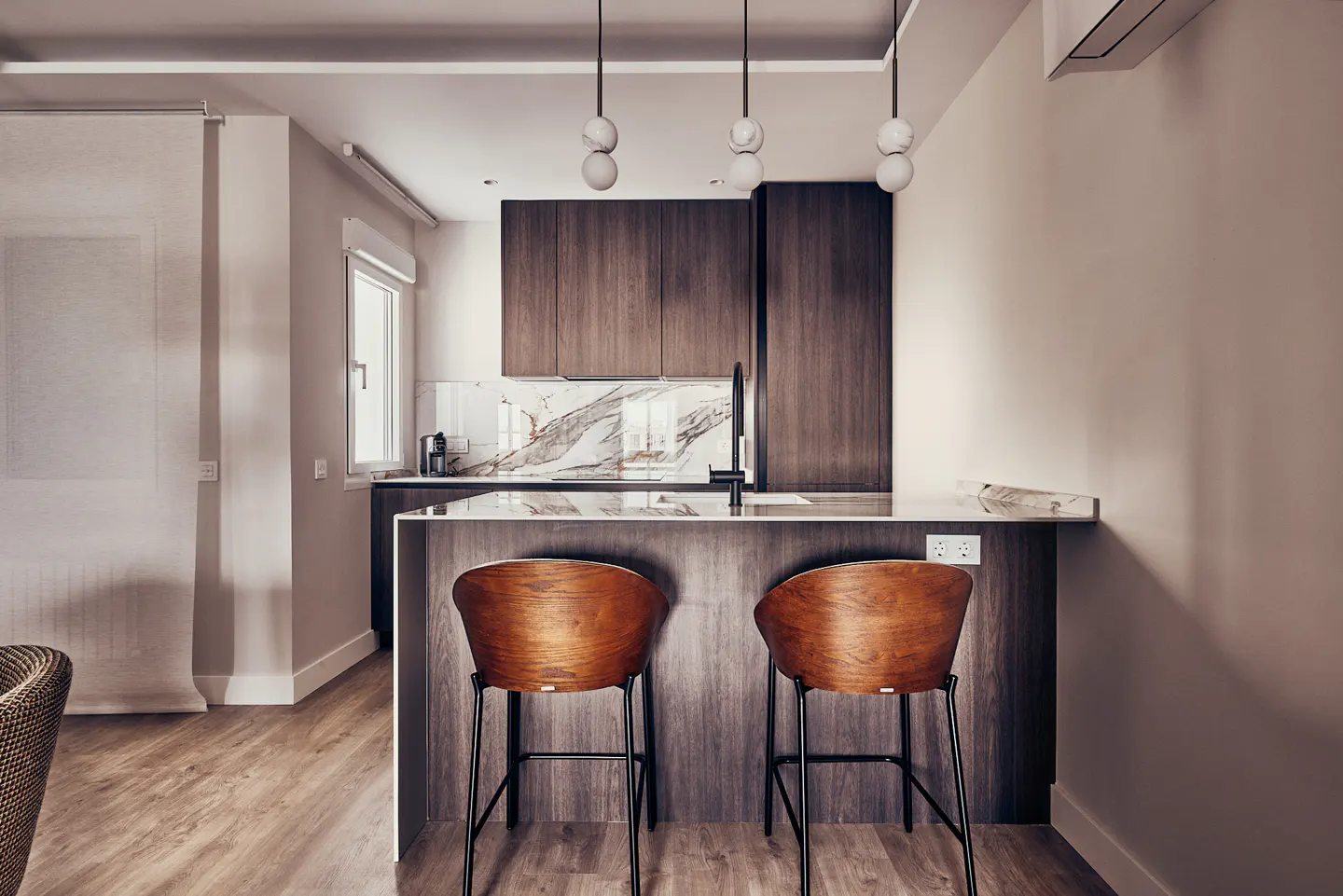 A modern kitchen with dark wood cabinets, marble backsplash, and two wooden bar stools at the island. Three pendant lights hang above.