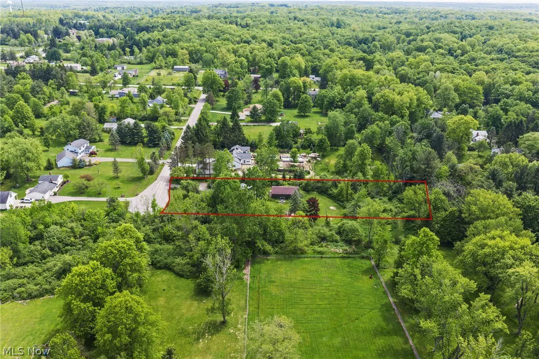 Aerial view of a wooded residential lot outlined in red, surrounded by lush green trees and nearby suburban homes.