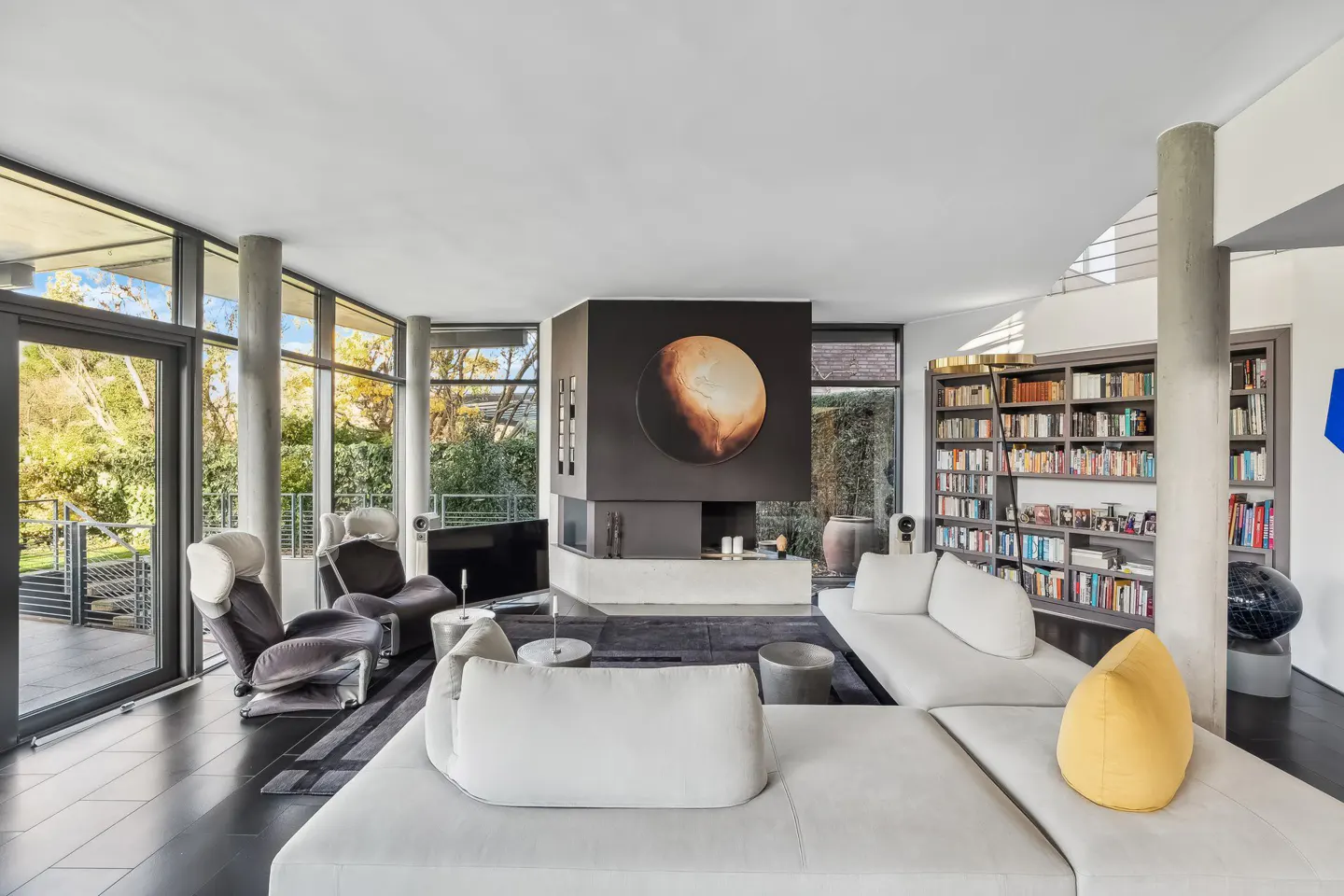 A modern living room with a white sectional sofa, gray chairs, and a black fireplace with a round art piece.