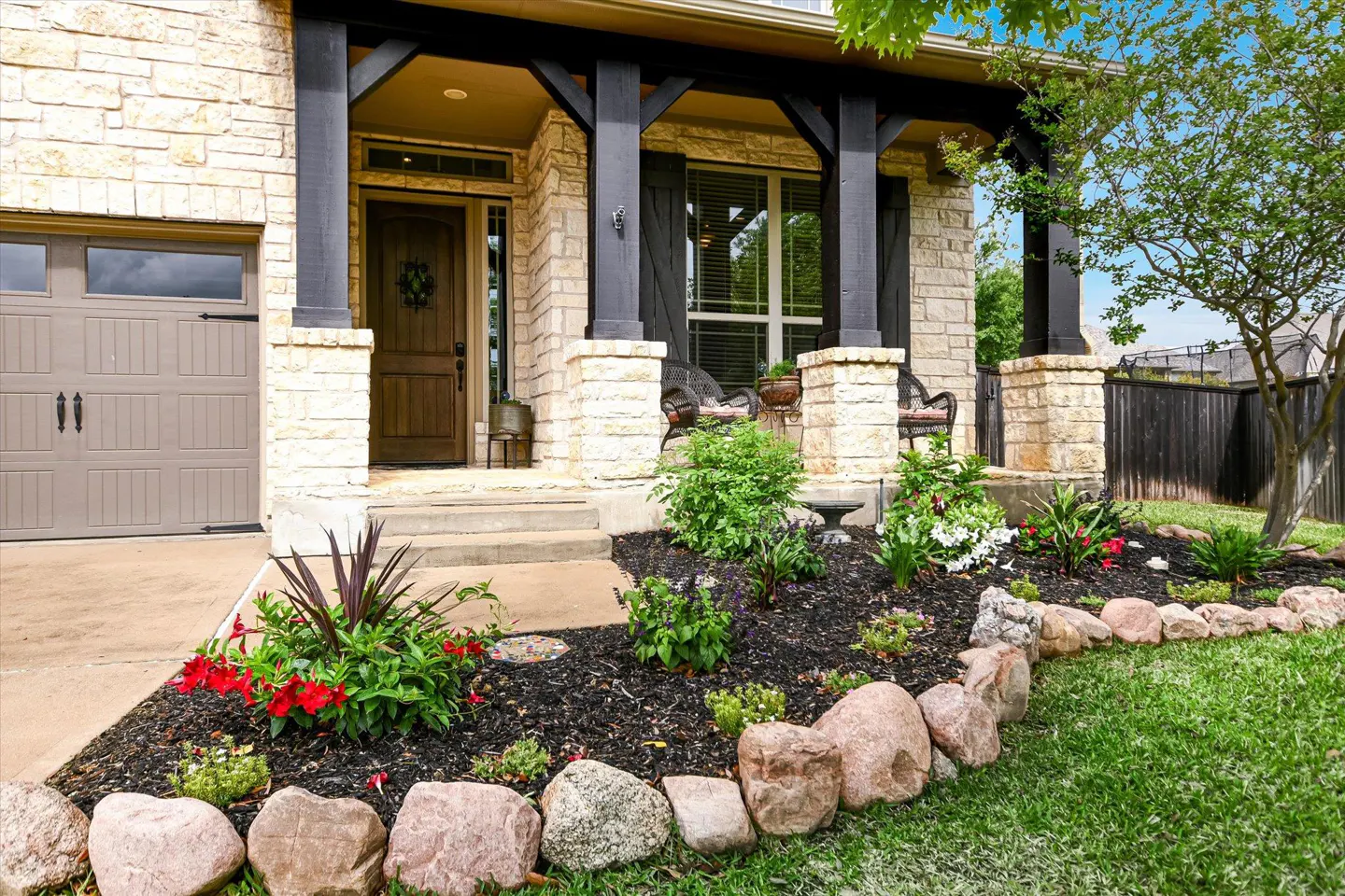 Exterior of a stone house with a brown front door, black pillars, and a landscaped garden.
