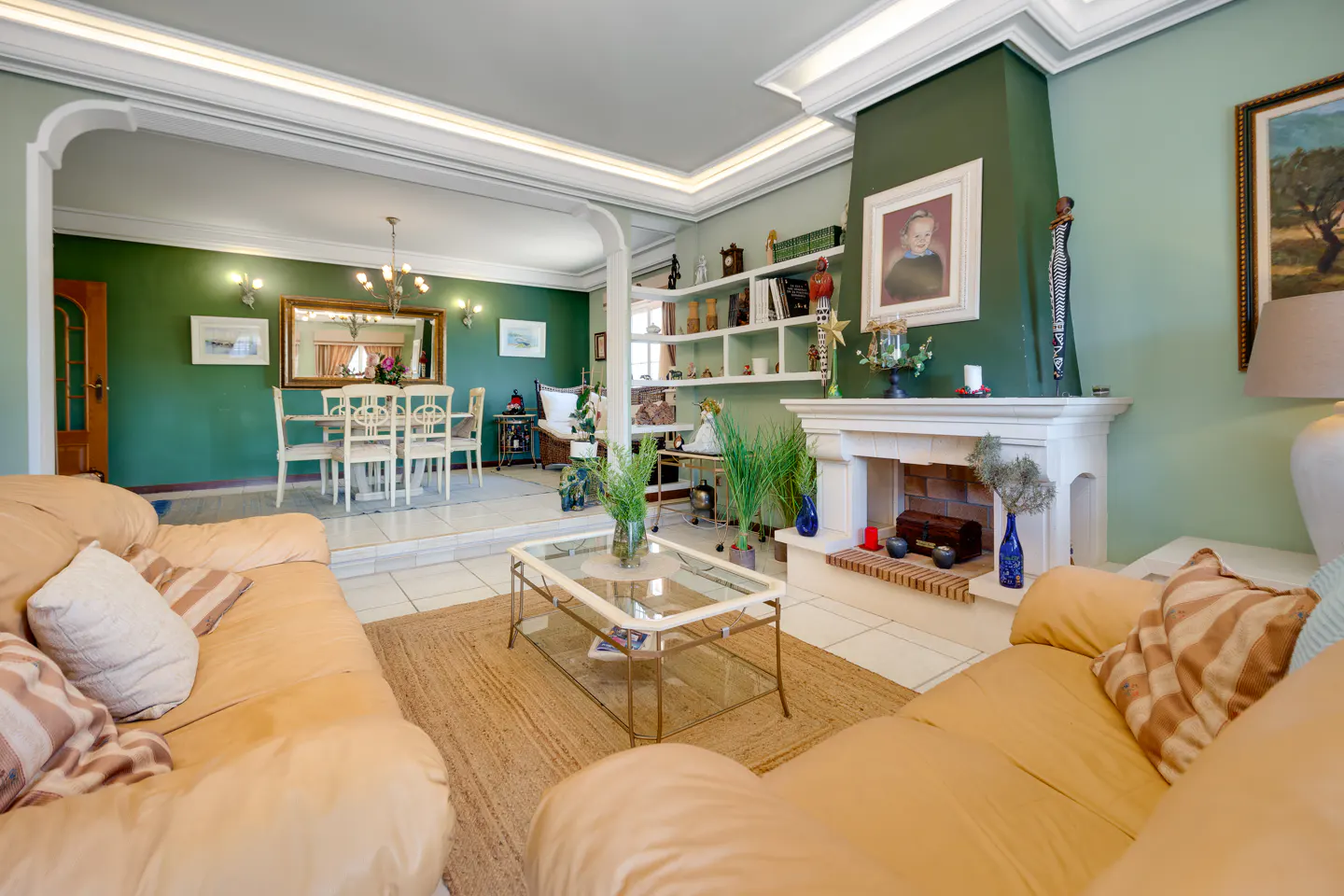 Living room with tan leather sofas, a glass coffee table on a jute rug, and a dining area with white chairs in the background.