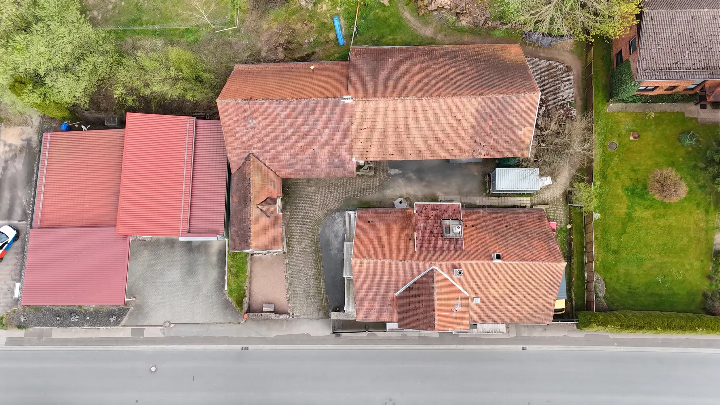 Aerial view of a property with red-tiled roofs, a paved courtyard, and green trees surrounding the buildings.