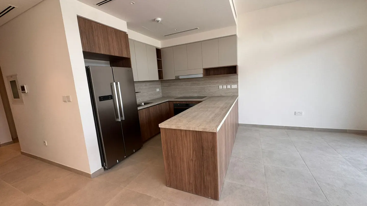 A modern kitchen with wood cabinets, stainless steel fridge, and gray countertops. The floor is tiled in gray.