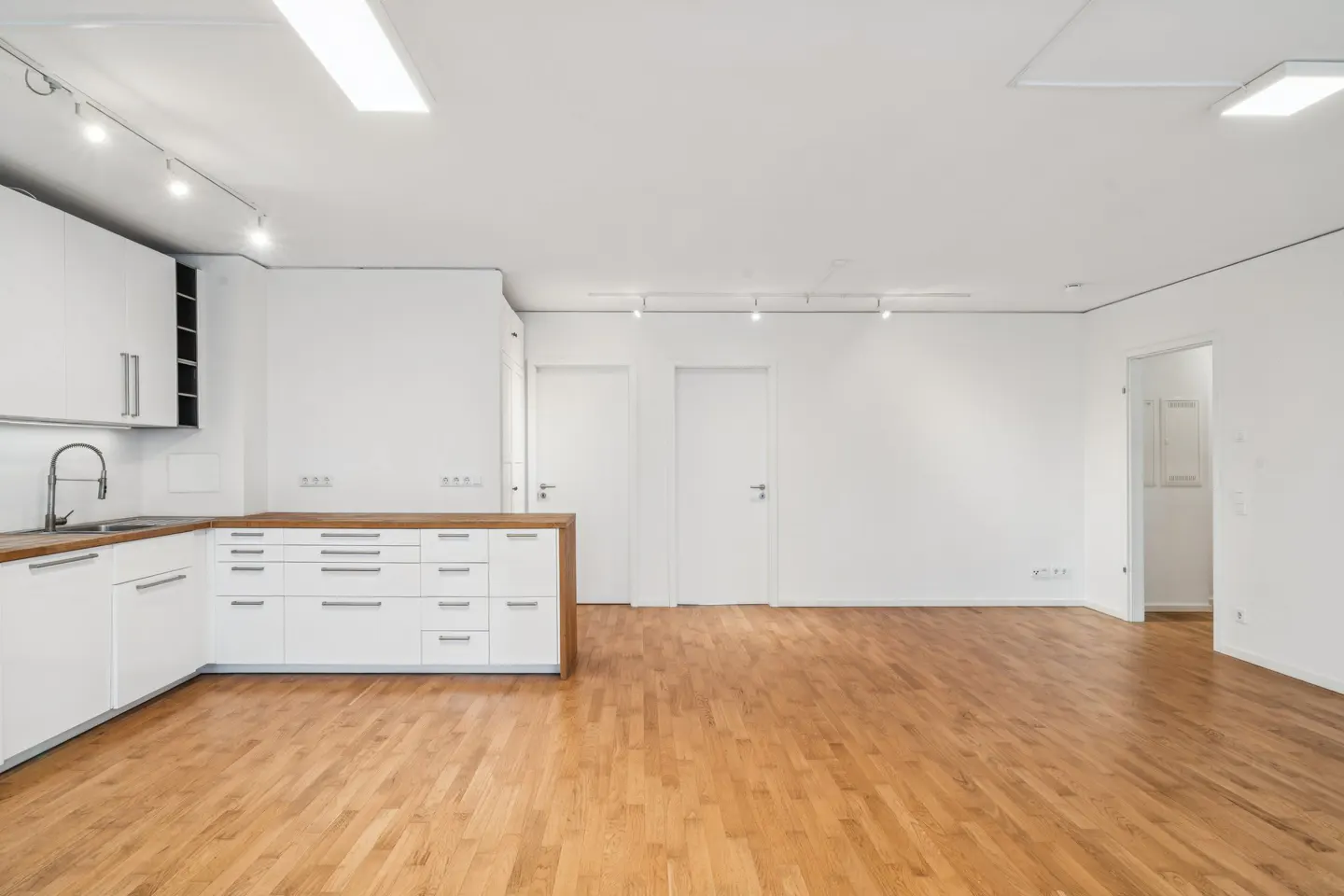 Bright, open-concept apartment with hardwood floors, white walls, and a modern white kitchen with wood countertops.