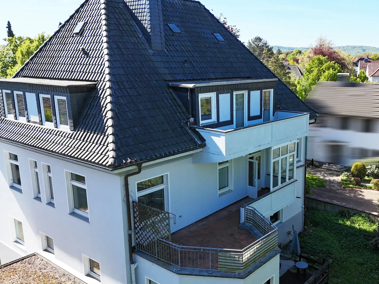 Aerial view of a light gray, multi-story house with a dark gray roof and multiple balconies.