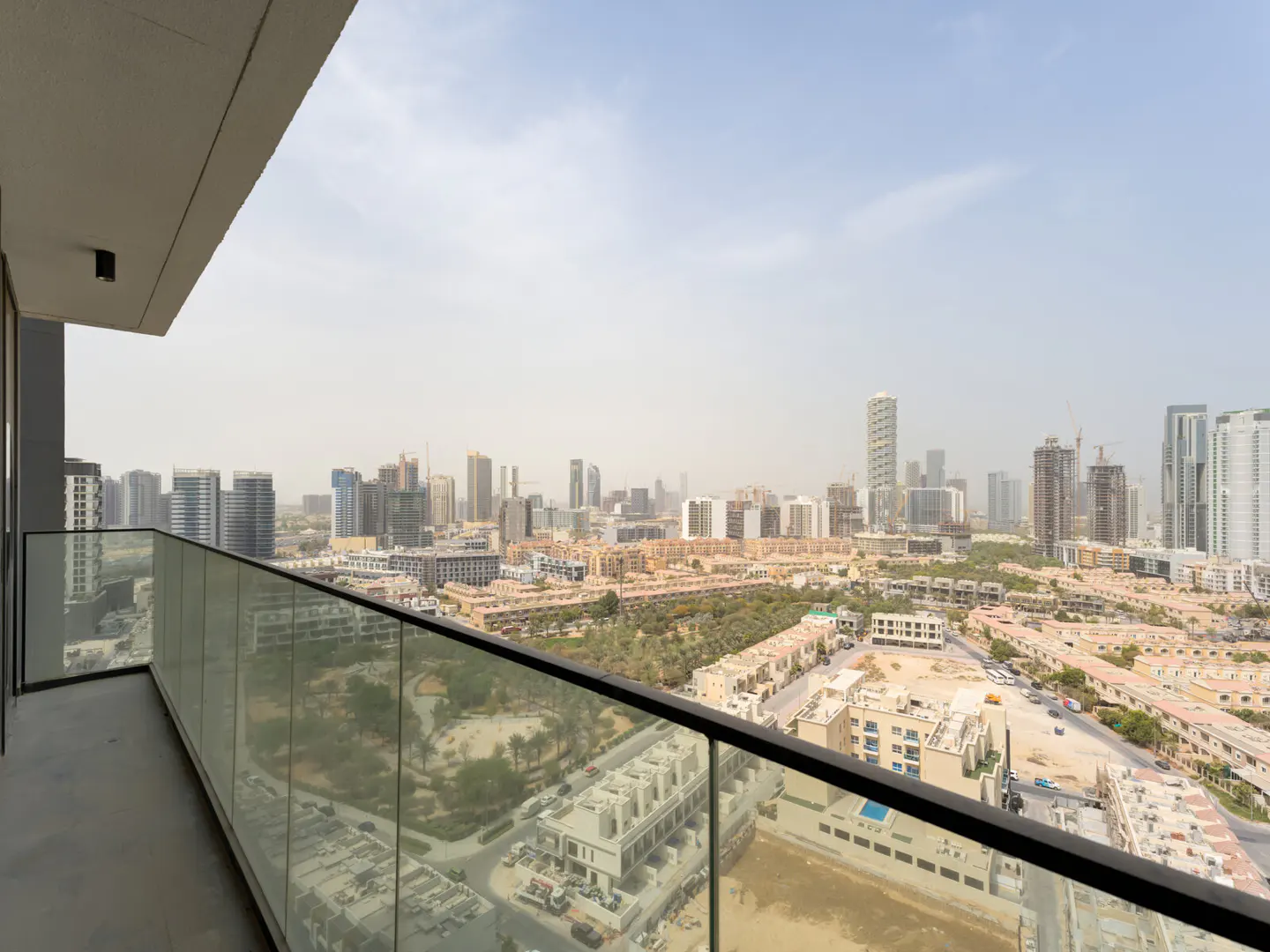 View from a balcony with glass railings overlooking a city with tall buildings.