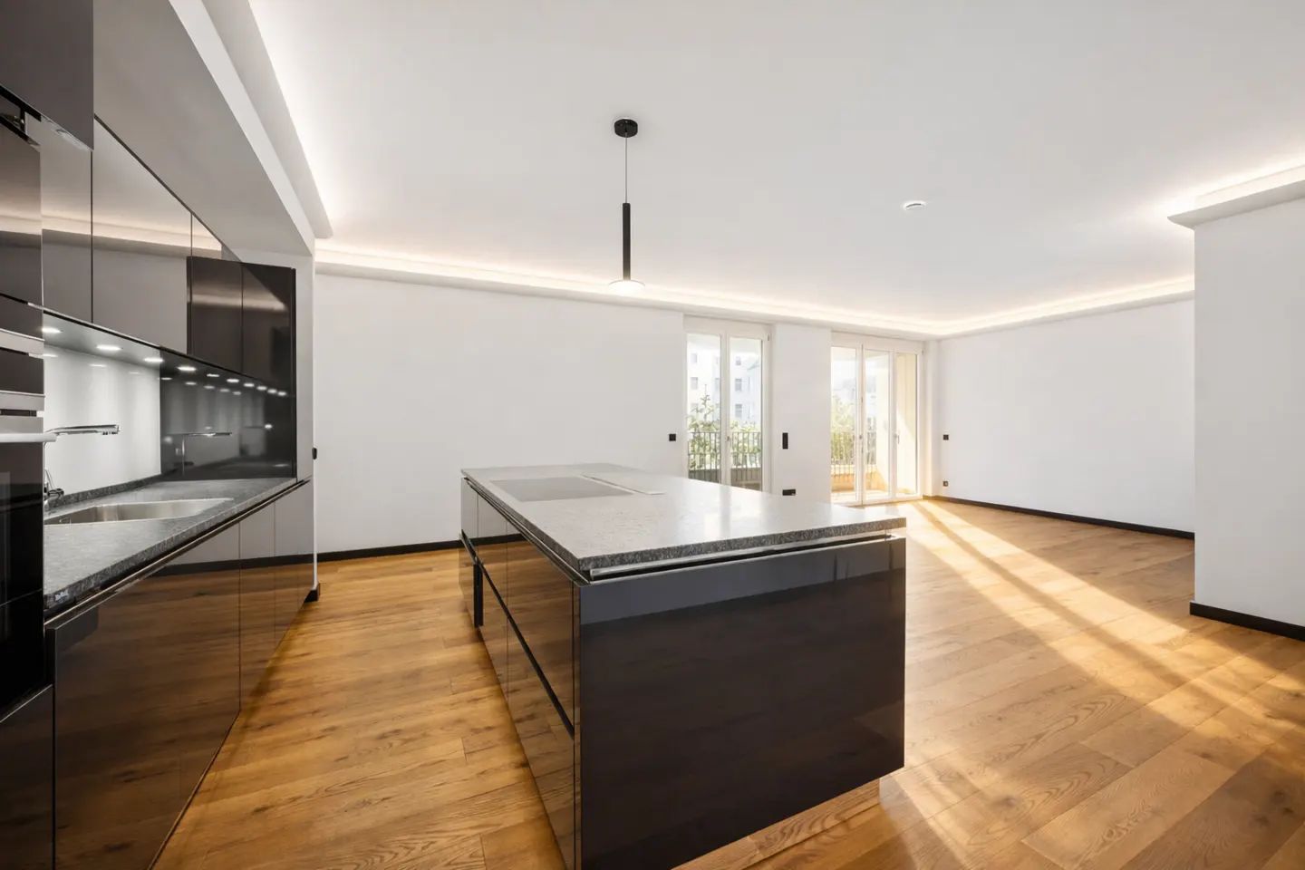 Bright, modern kitchen with black cabinets, island, wood floors, and white walls. Light streams in from balcony doors.