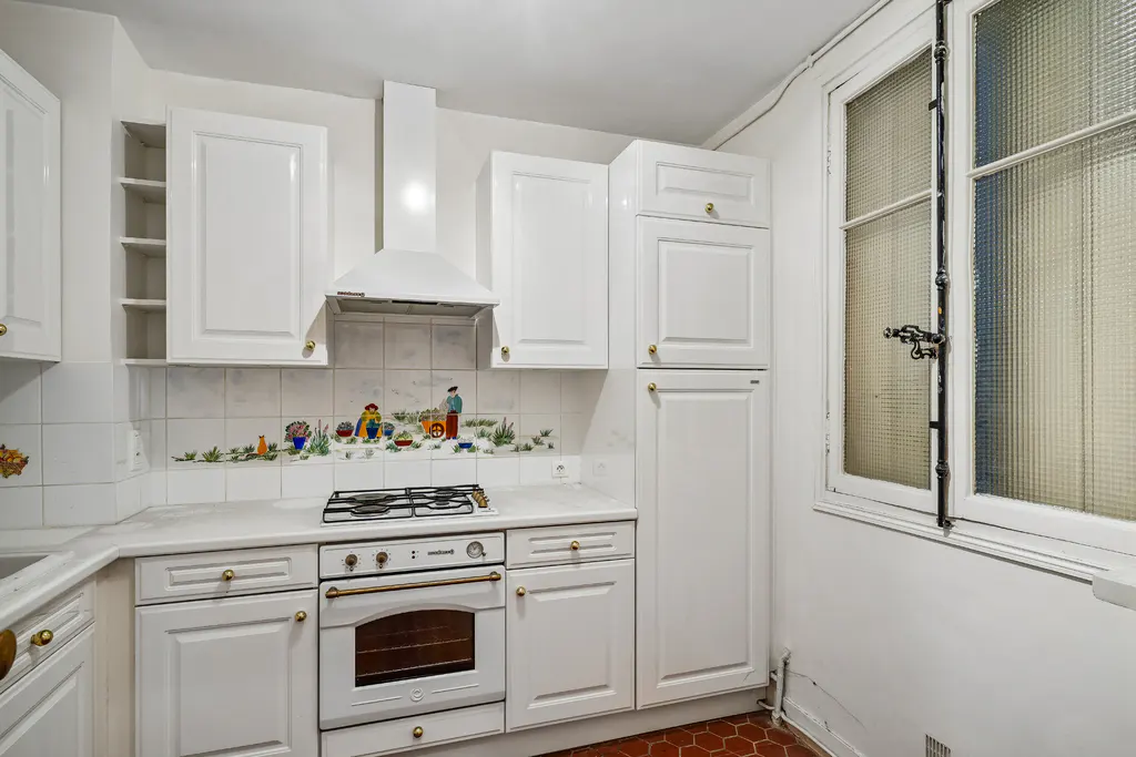 A small kitchen with white cabinets, a white stove, and a window with textured glass.