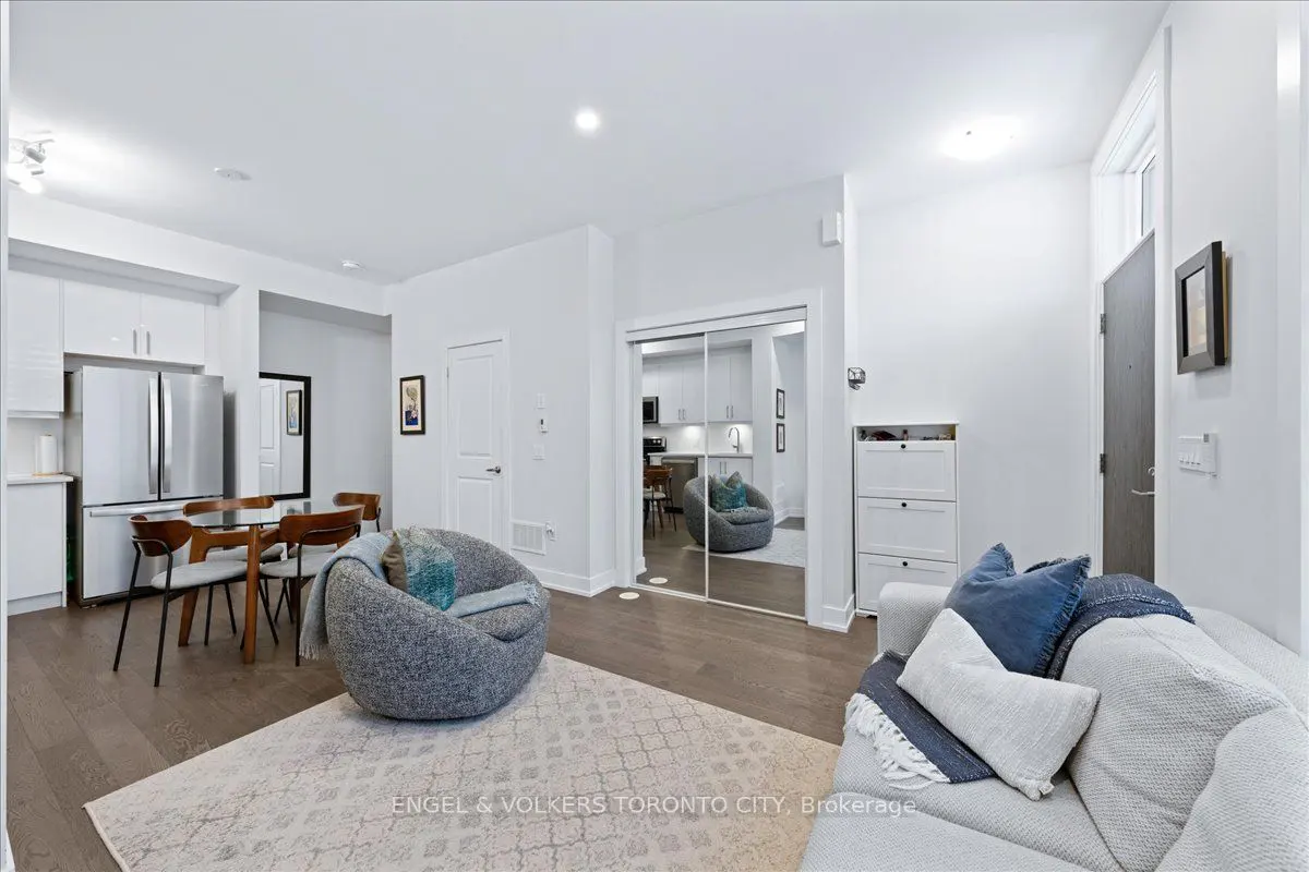 Bright, modern condo living room with white walls, wood floors, and a gray beanbag chair. A dining table and sofa add comfort.