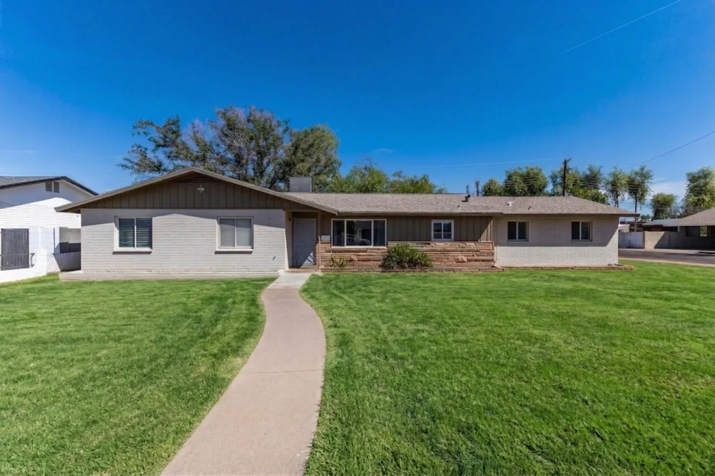 A single-story house with a green lawn and a curved walkway under a clear blue sky.