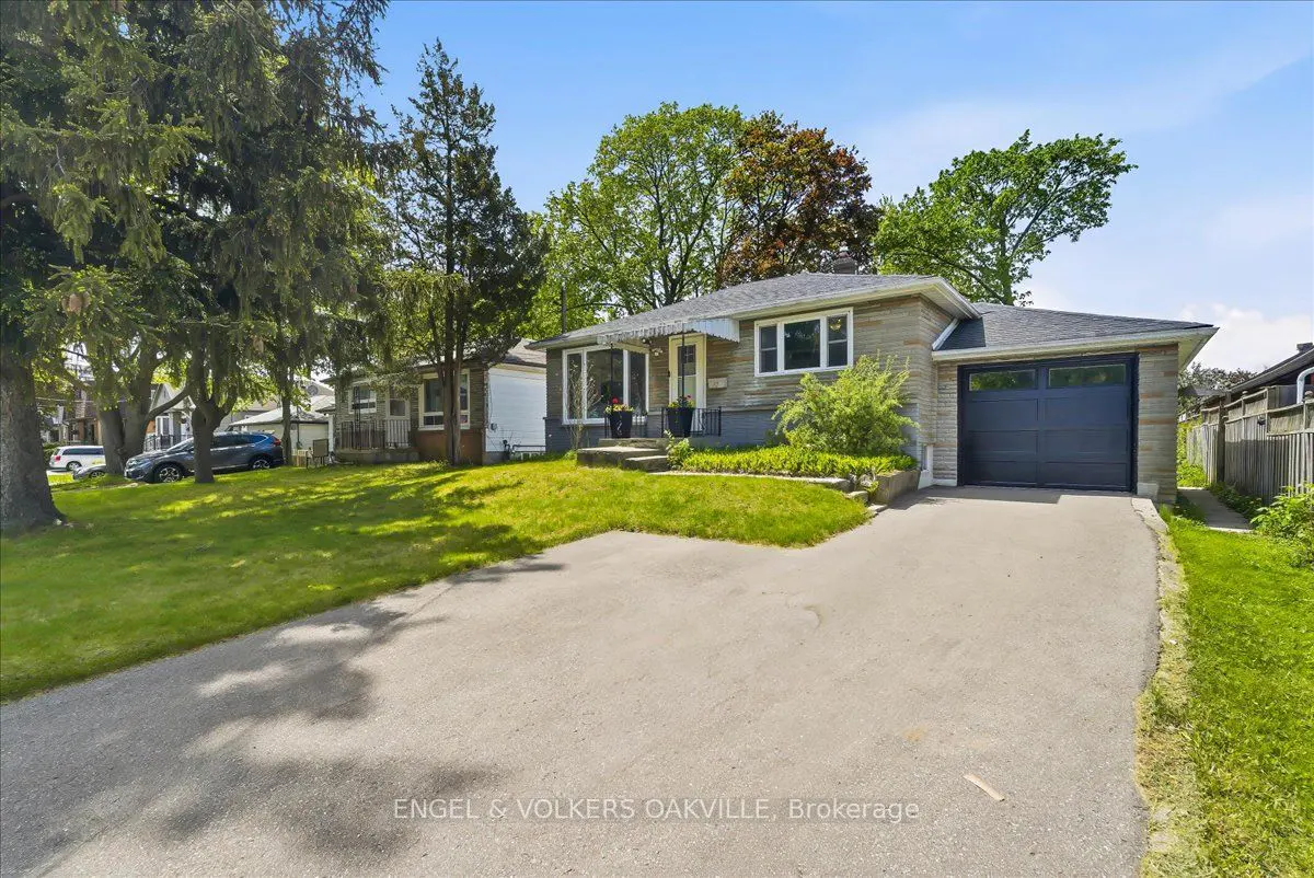A single-story stone house with a dark garage door, green lawn, and trees under a blue sky.