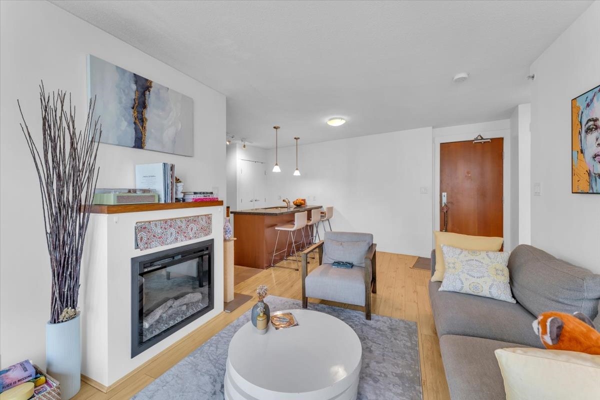 A bright living room with a fireplace, gray sofa, and a round white coffee table on a gray rug. The kitchen island is visible in the background.