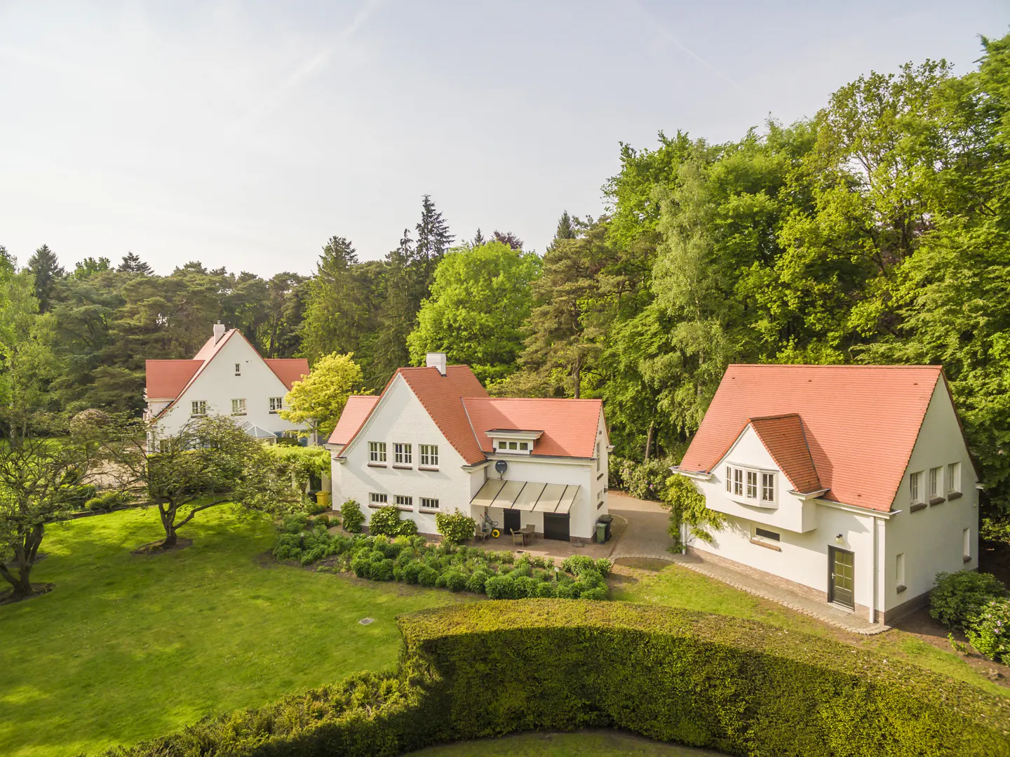 Aerial view of three white houses with red roofs, surrounded by green lawns and trees.