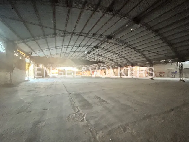 A large, empty warehouse with a high, arched metal roof and concrete floor.