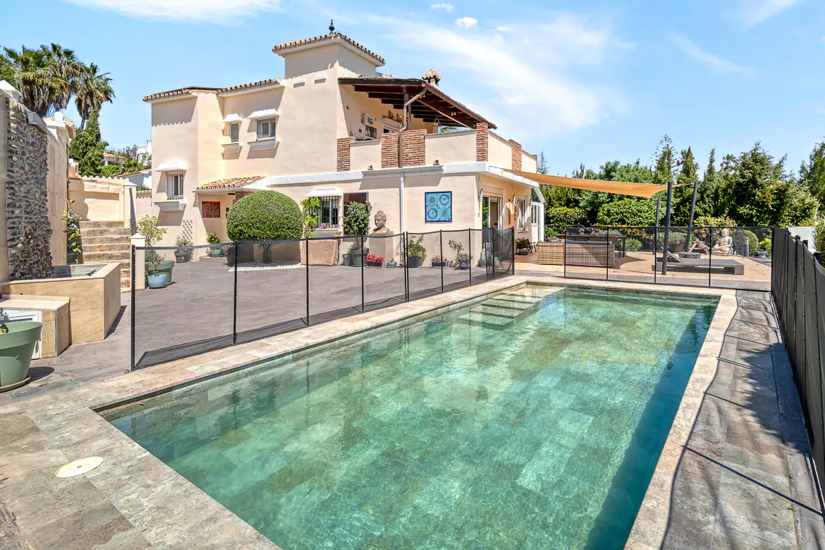 A tan two-story house with a pool in the backyard on a sunny day.