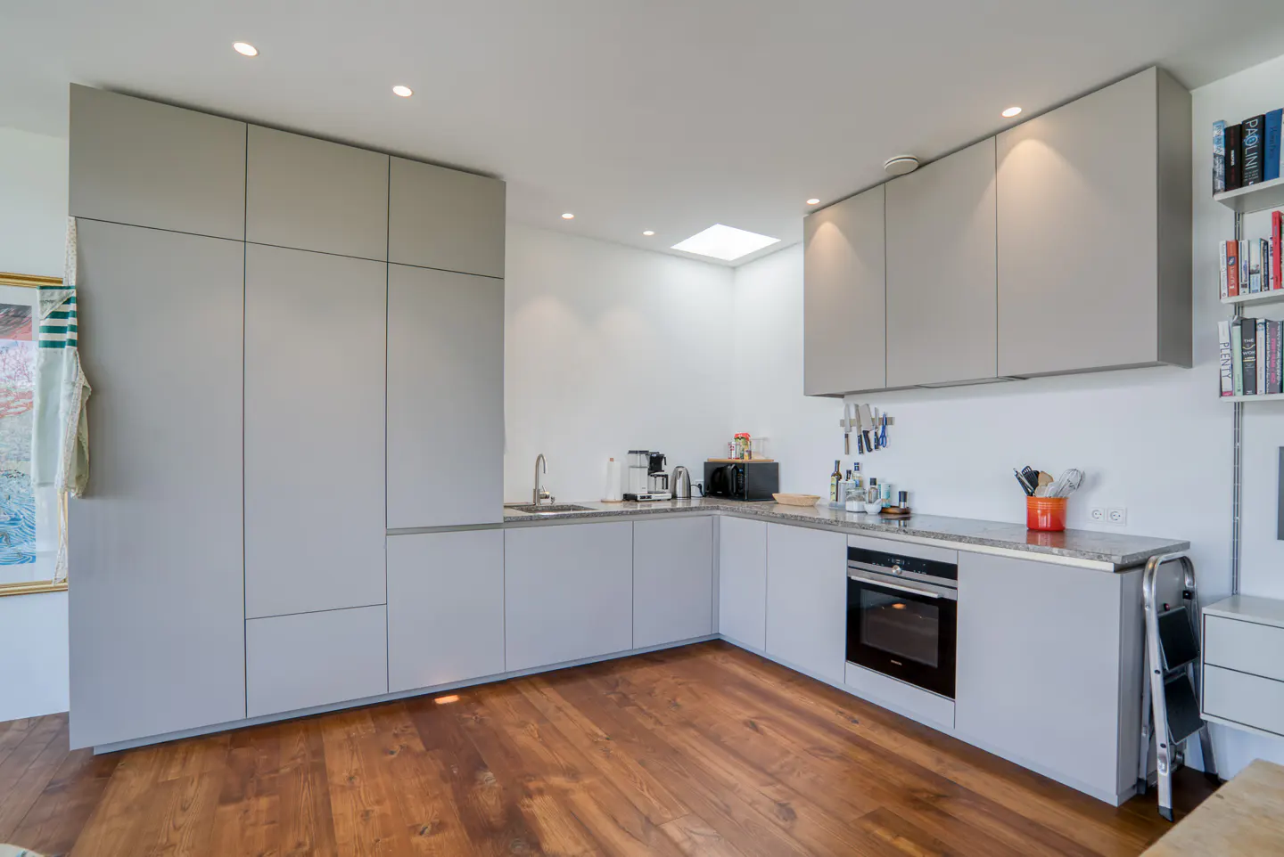 Bright kitchen with gray cabinets, granite countertops, and wood floors. Appliances and a ladder are visible.