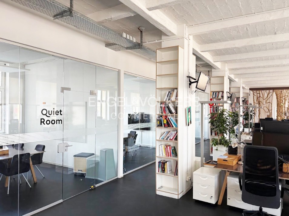 Modern office interior with a glass-walled "Quiet Room," tall bookshelves, and workstations with black chairs on dark floors.