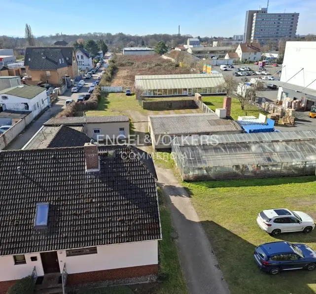 Aerial view of a commercial property with greenhouses, buildings, and parking. Engel & Völkers Commercial logo is visible. Cars parked on the grass.