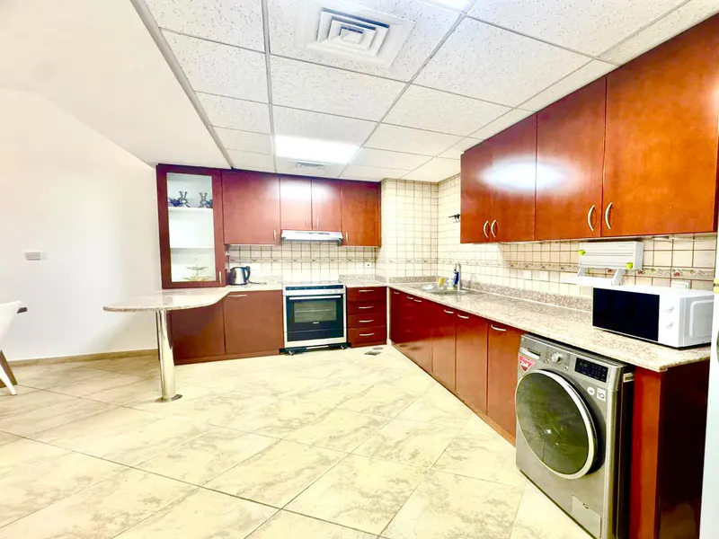 A kitchen with brown cabinets, beige tile floor, and appliances. A washing machine is on the right.