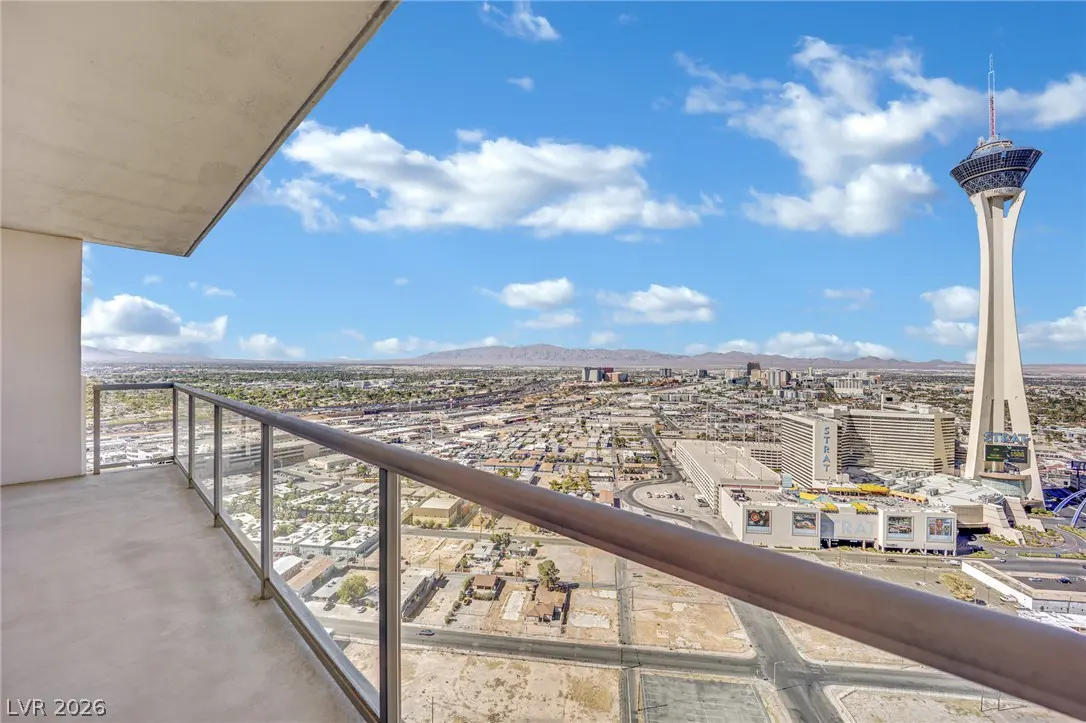 View from a balcony with glass railings overlooking the Las Vegas skyline and the Stratosphere tower on a sunny day.