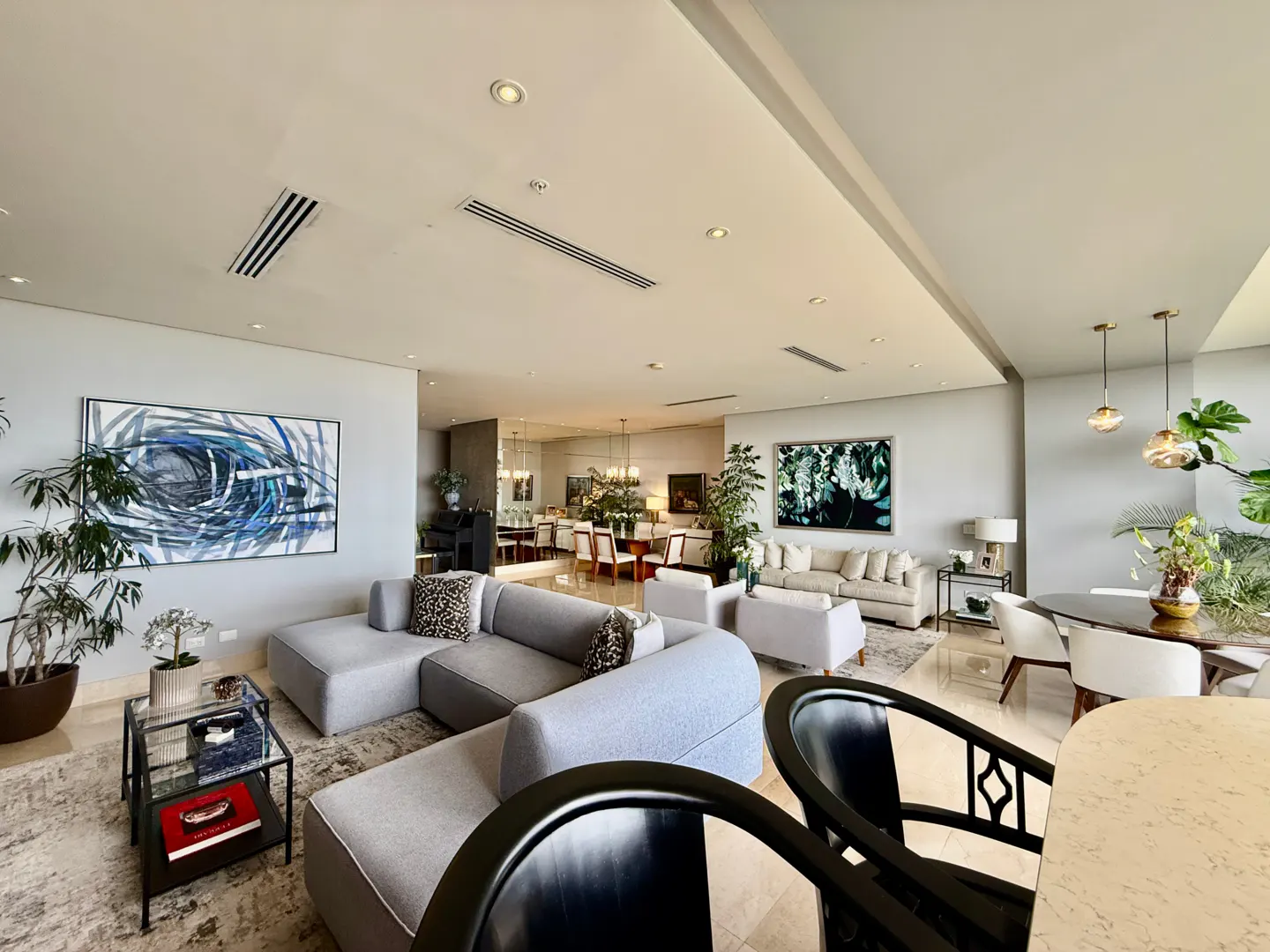 A modern, open-concept living space with gray sofas, abstract art, and a dining area in the background. Plants add a touch of nature.