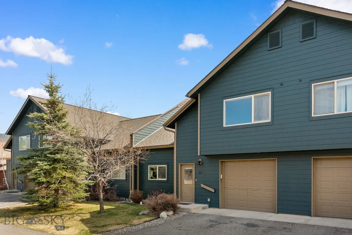 Exterior of a two-story, blue townhouse with brown garage doors and a blue sky.