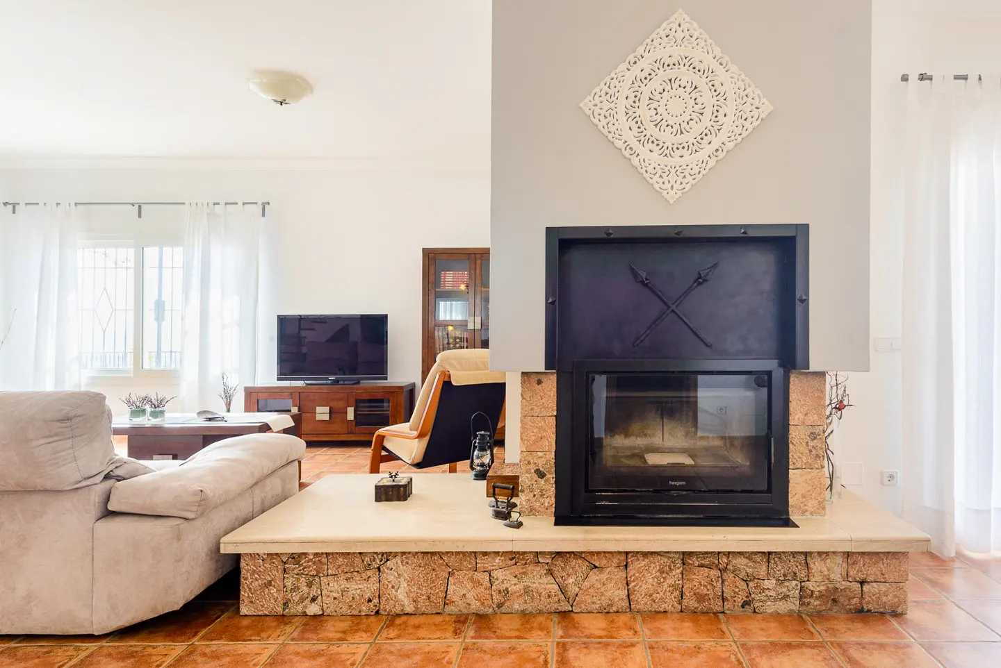 Living room with a stone fireplace, black metal accents, and a decorative white wall hanging. A beige sofa and TV are visible.