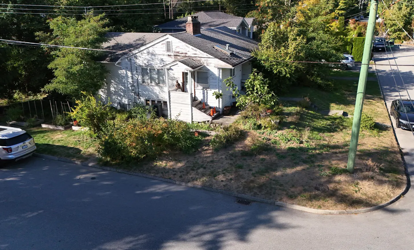 A two-story white house with a chimney, surrounded by trees and a lawn, sits on a corner lot.