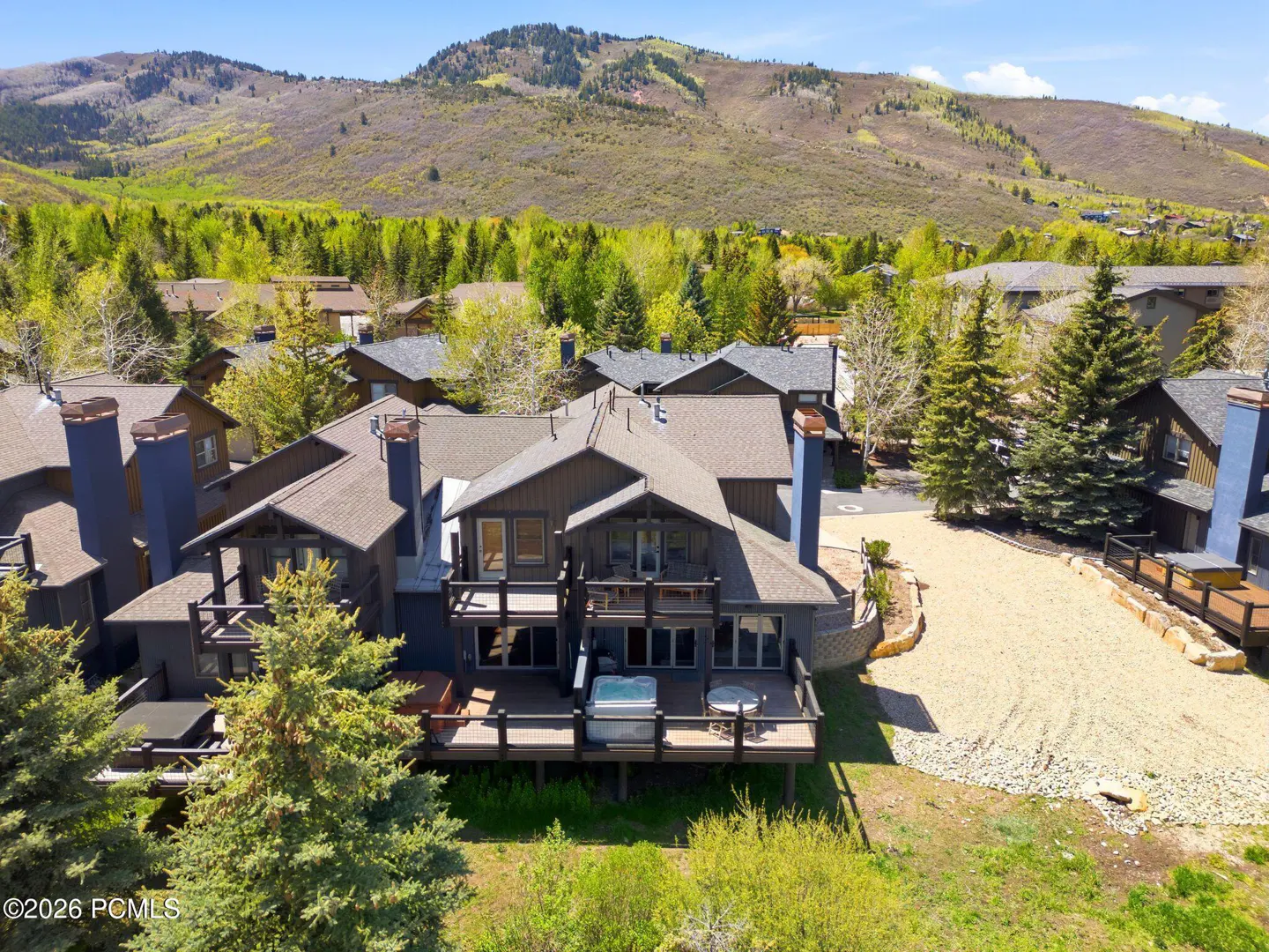 Aerial view of a gray two-story house with a deck, hot tub, and mountain backdrop.