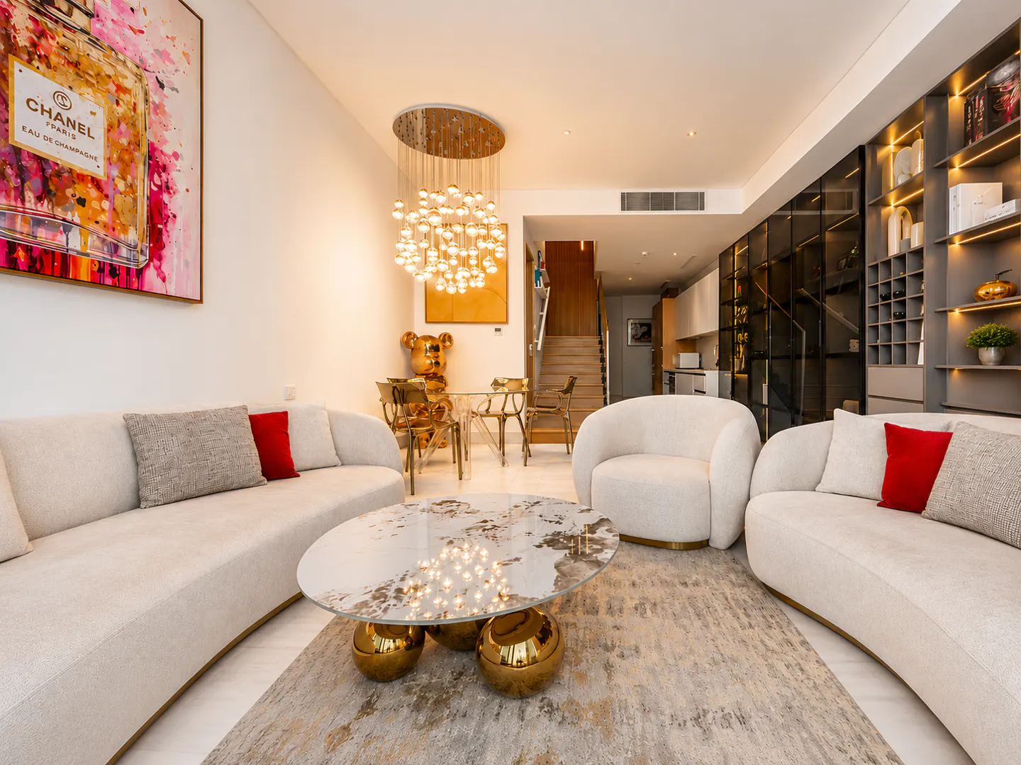 Modern living room with cream sofas, a marble coffee table with gold spheres, a bubble chandelier, and Chanel wall art.