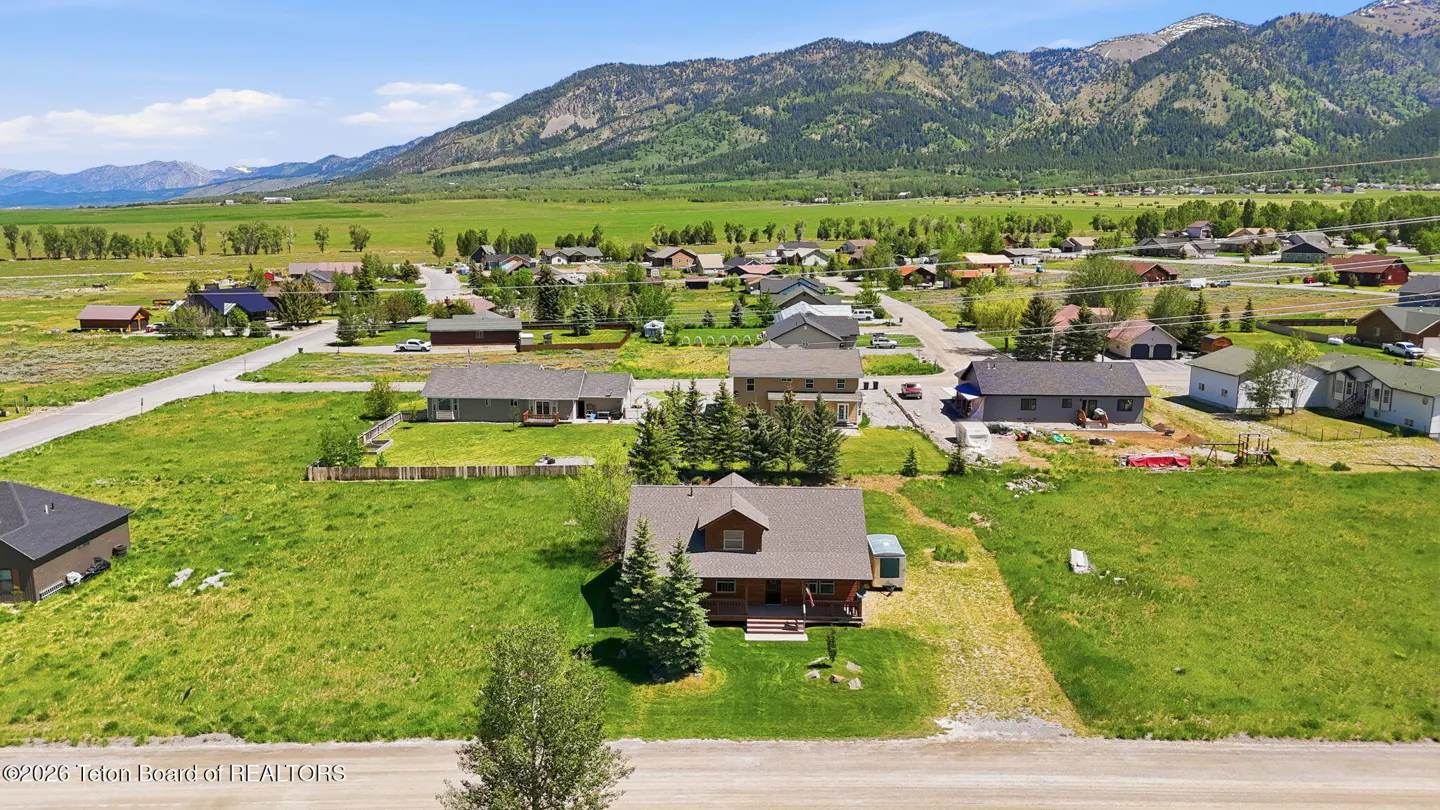 Aerial view of a brown house on a large grassy lot in a residential neighborhood with mountains in the background.