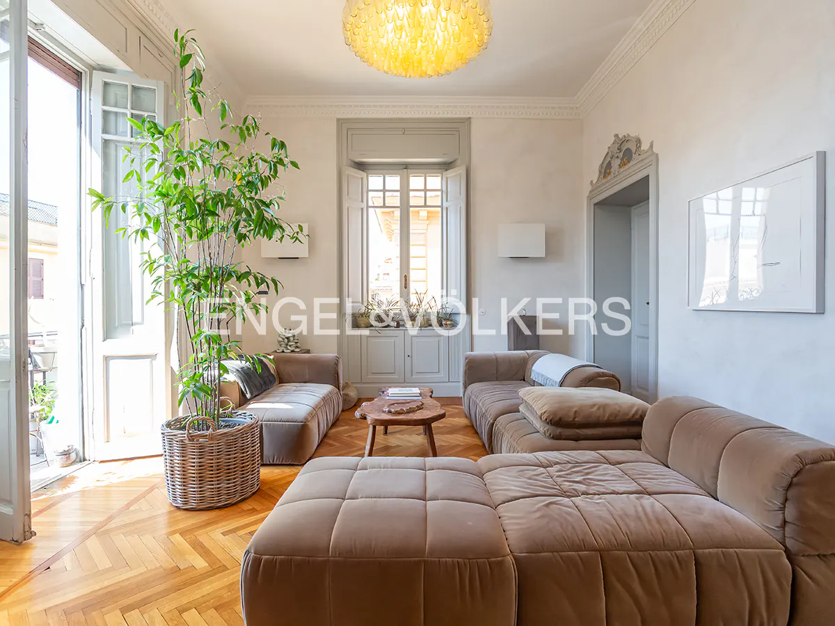 Living room with parquet floors, a large brown sectional sofa, and a tall potted plant near an open door.