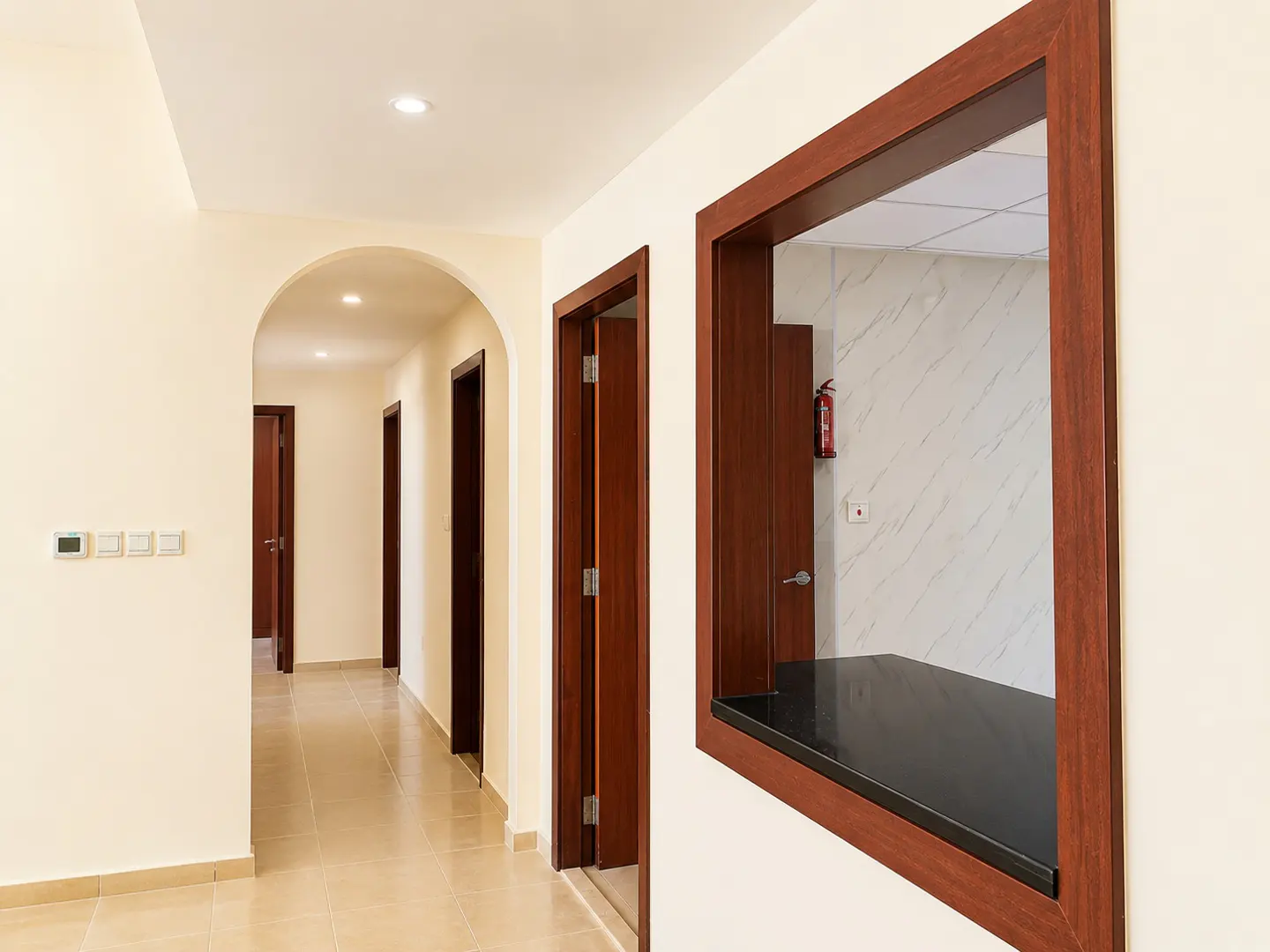 Hallway with beige walls, brown doors, and tile floors. A dark countertop is framed by a wood window.