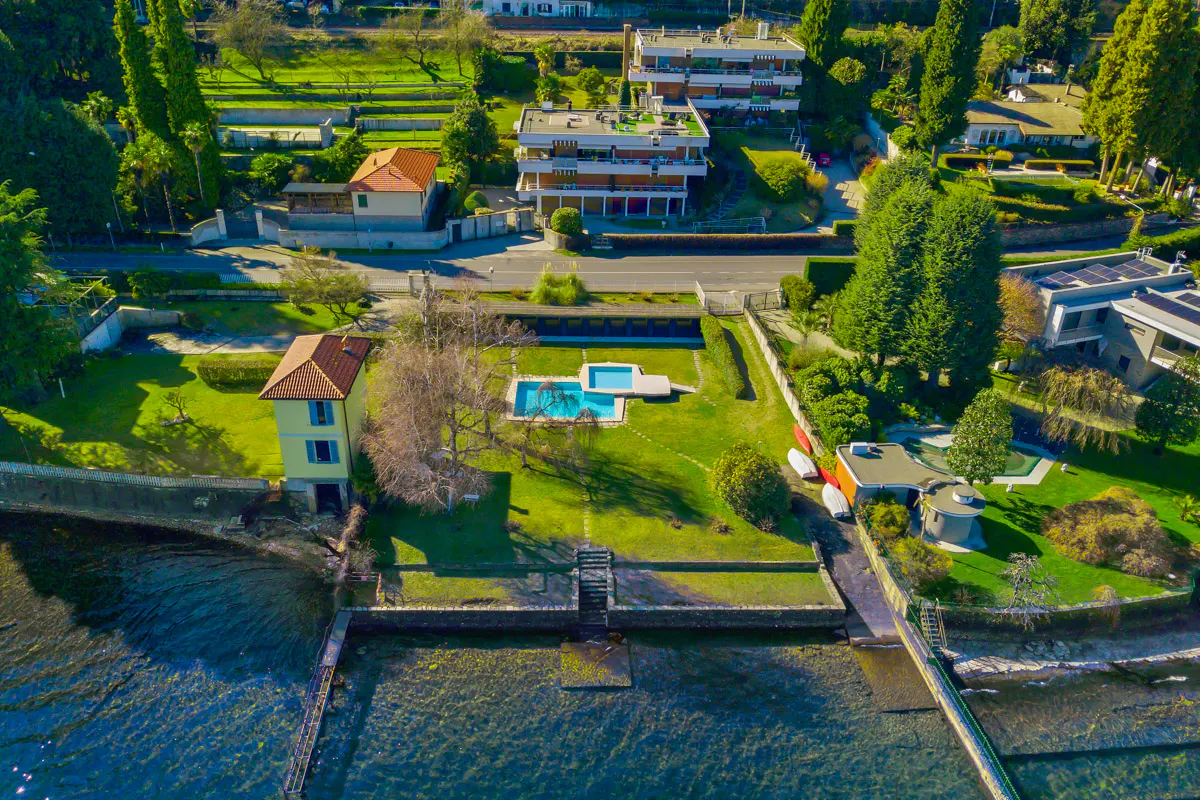 Aerial view of a lakeside property with a pool, green lawn, and a yellow house with a red tile roof.