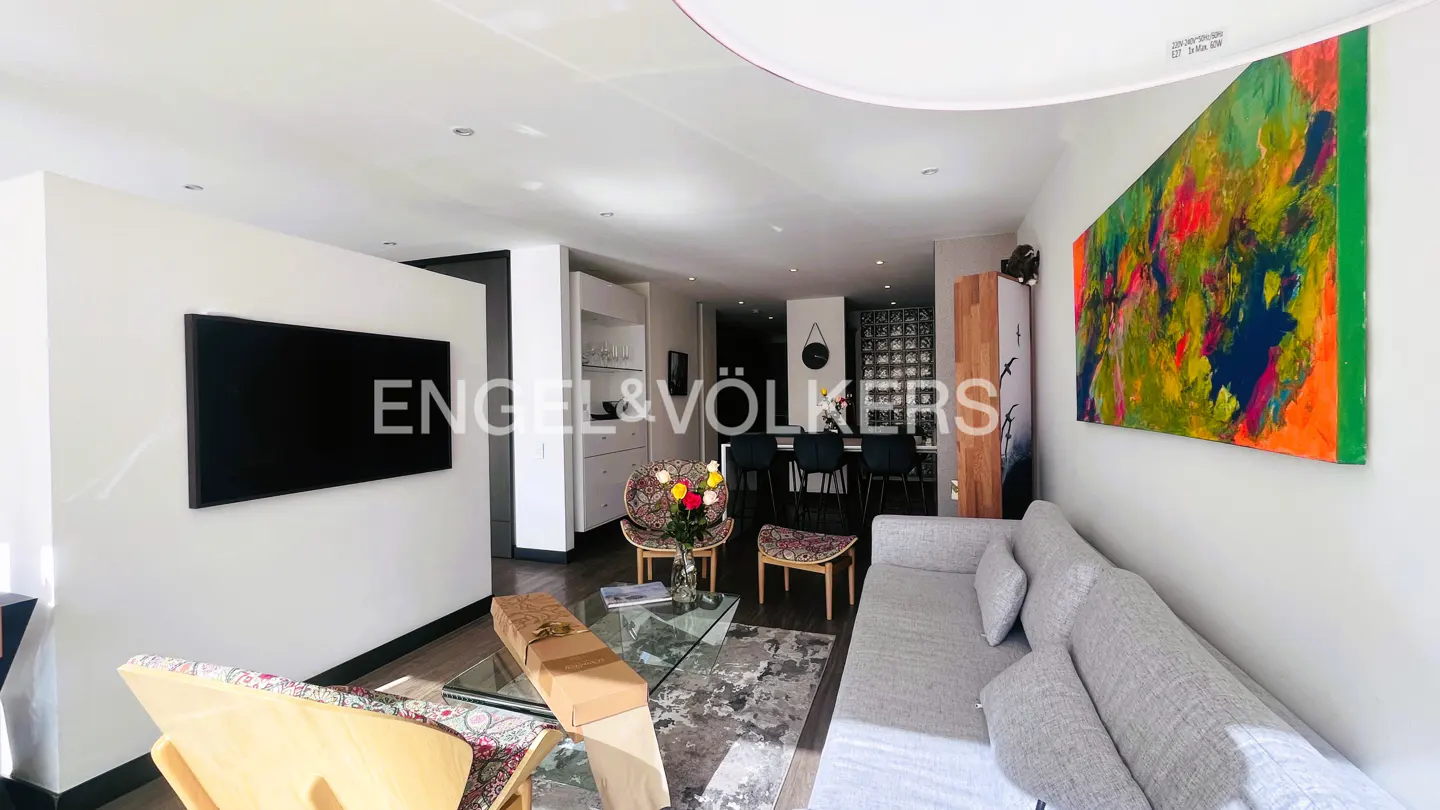 Modern living room with a grey sofa, glass coffee table, patterned accent chairs, and a vibrant abstract painting on the wall.