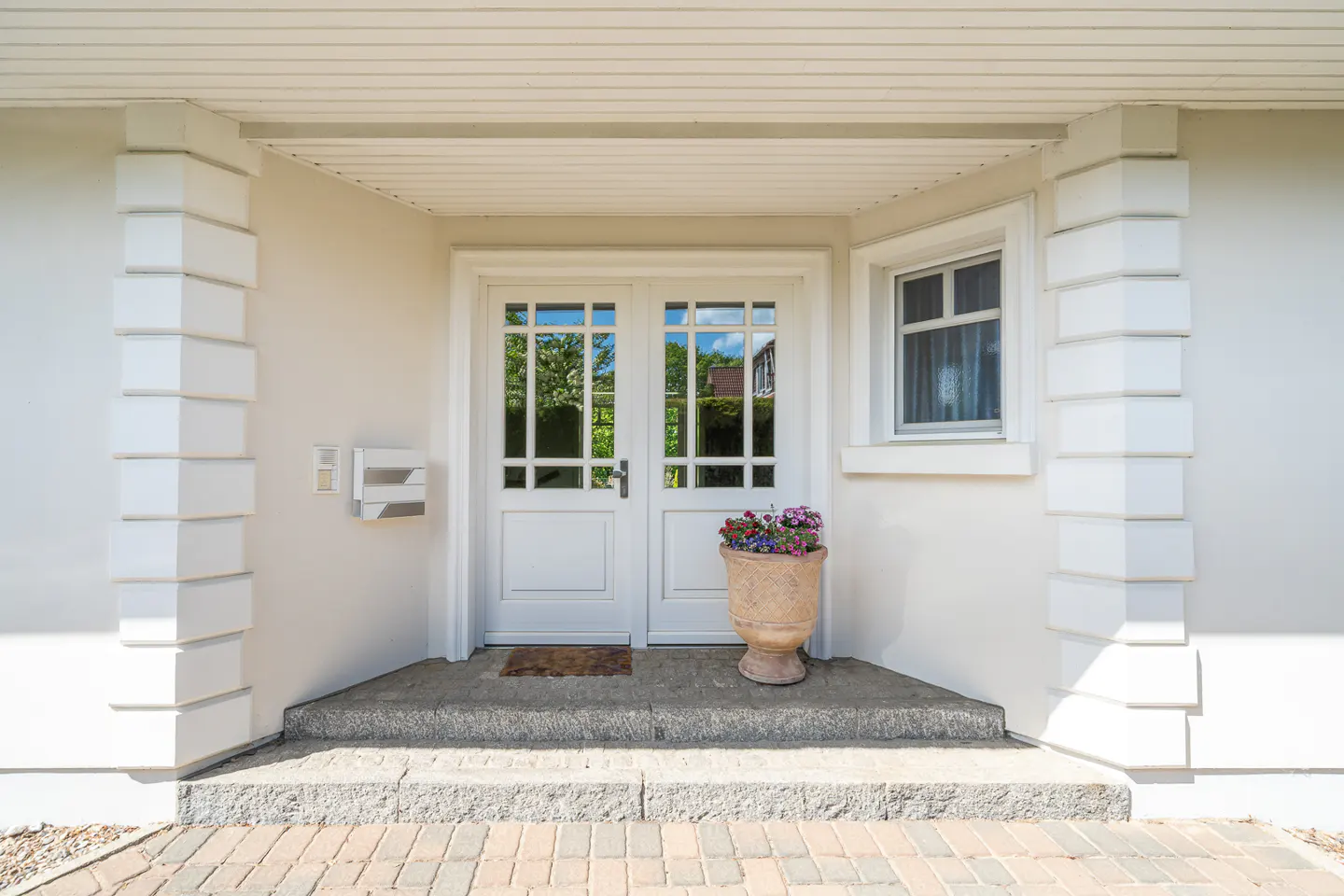 White double front doors with glass panes, a small window, and a flower pot on the porch of a white house.