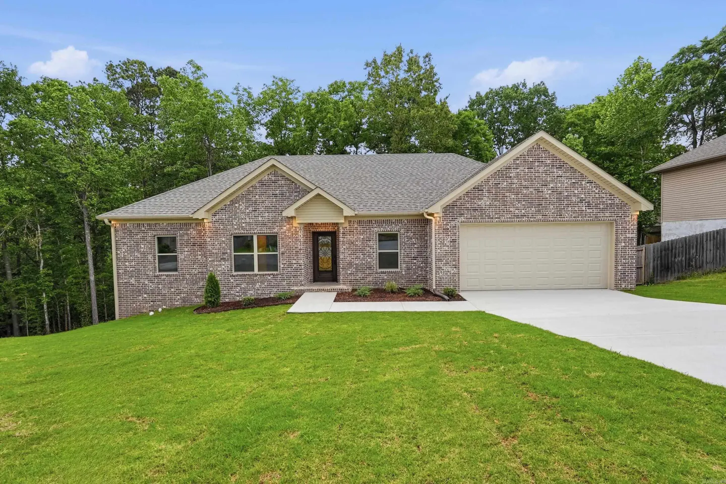 A single-story brick house with a gray roof, a two-car garage, and a green lawn. Trees are in the background.