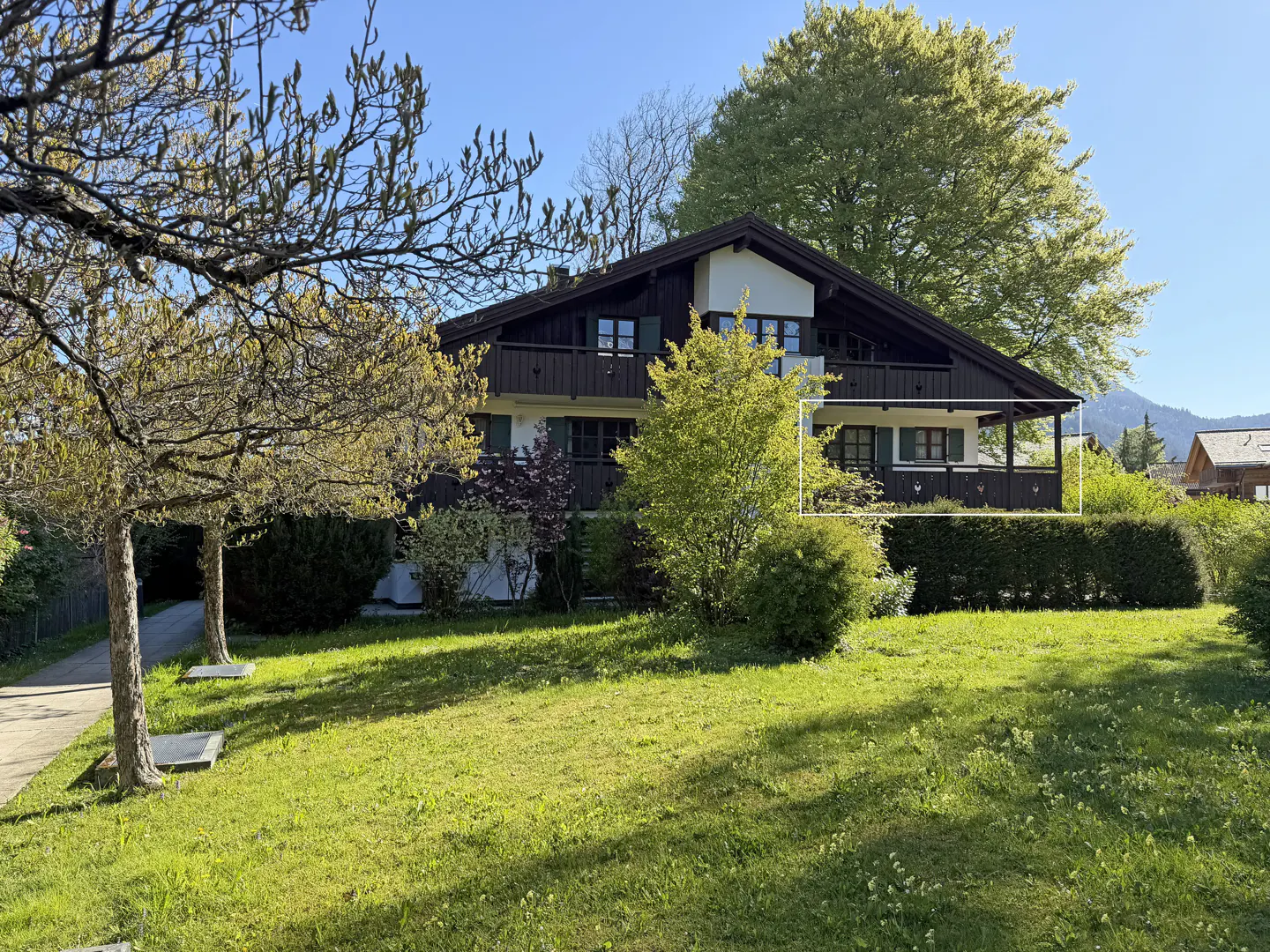 Two-story house with dark brown trim and green shutters, surrounded by trees and a green lawn.