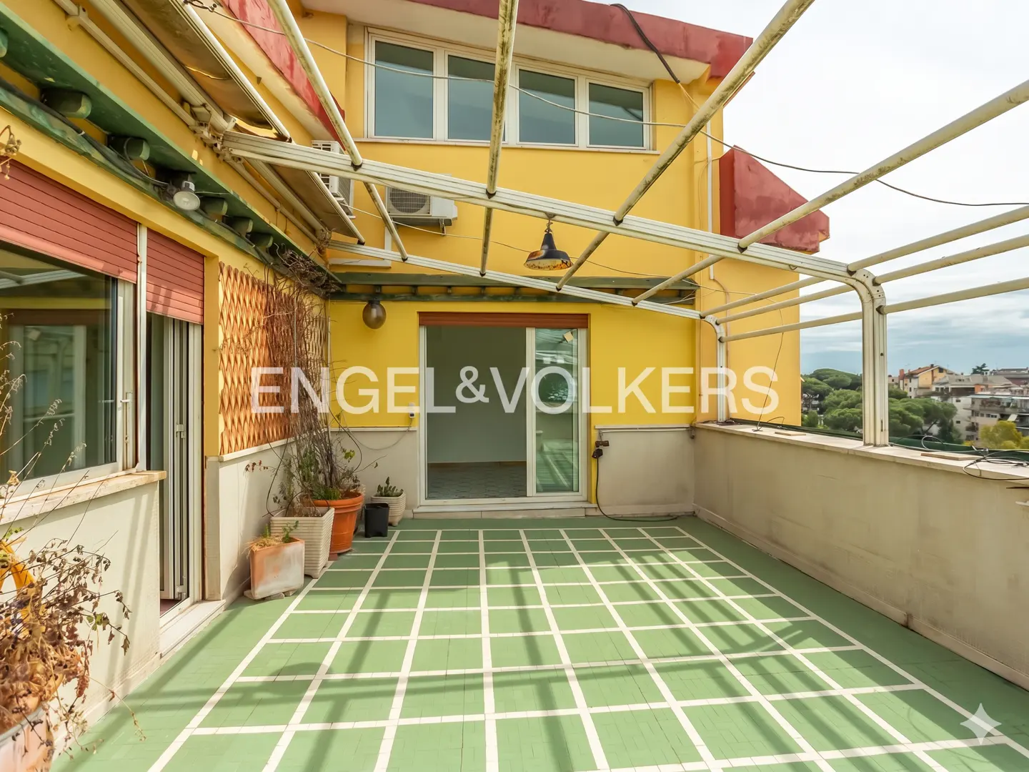 A sunny balcony with a green and white tiled floor, yellow walls, and a metal pergola. Engel & Volkers logo is visible.