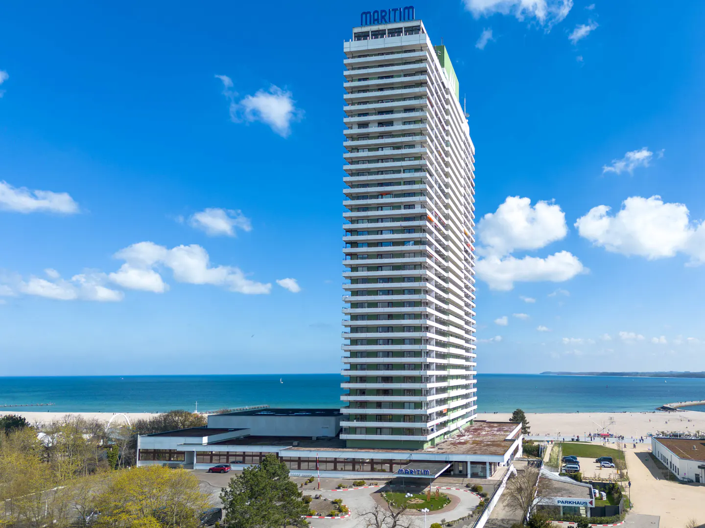 Tall white Maritim hotel tower on a beach, under a blue sky with scattered clouds.